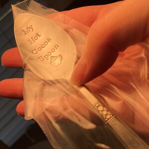 May include: A silver spoon with the words "My Hot Cocoa Spoon" engraved on it. The spoon is in a clear plastic bag.
