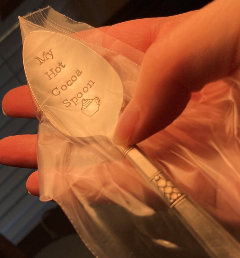 May include: A silver spoon with the words "My Hot Cocoa Spoon" engraved on it. The spoon is in a clear plastic bag.