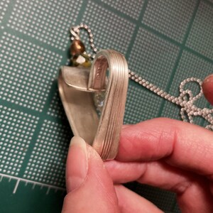 May include: A silver heart-shaped pendant necklace made from a repurposed spoon. The pendant has a textured surface and is attached to a silver chain.