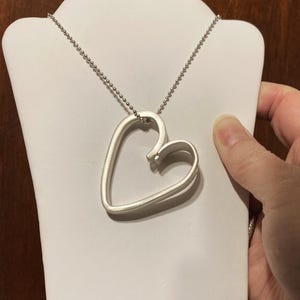 May include: A silver necklace with a double heart pendant. The heart is open and the chain is silver.
