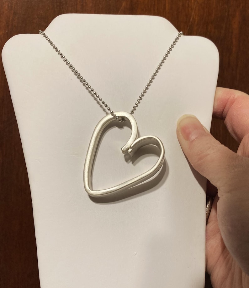 May include: A silver necklace with a double heart pendant. The heart is open and the chain is silver.