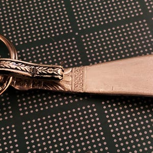 May include: A silver shoe horn keychain with an ornate design and a key ring.