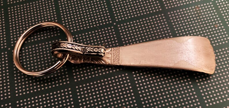 May include: A silver shoe horn keychain with an ornate design and a key ring.