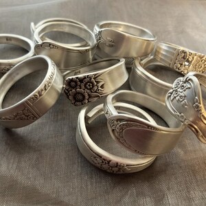 Puede incluir: Una colecci&oacute;n de nueve anillos de cuchara de plata, cada uno con un dise&ntilde;o &uacute;nico. Algunos anillos presentan patrones florales, mientras que otros tienen un dise&ntilde;o m&aacute;s simple. Todos los anillos est&aacute;n hechos de cubiertos reciclados.