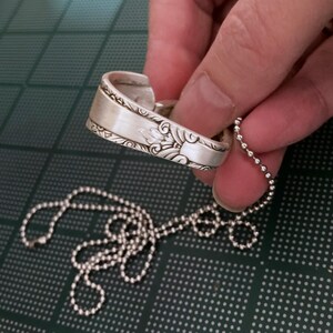 Puede incluir: Un collar de plata con una cuchara decorativa y una cadena de bolas.