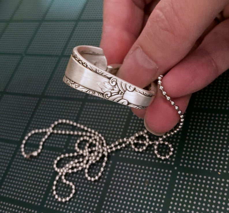 Puede incluir: Un collar de plata con una cuchara decorativa y una cadena de bolas.