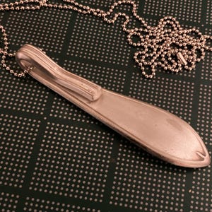May include: A silver spoon necklace with a ball chain. The spoon is bent into a unique shape and has a smooth, polished finish.