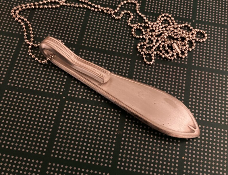 May include: A silver spoon necklace with a ball chain. The spoon is bent into a unique shape and has a smooth, polished finish.