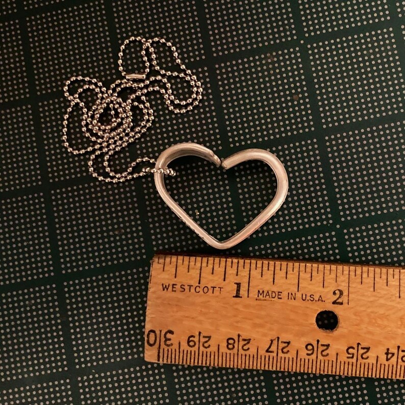 Puede incluir: Un collar de plata con un colgante en forma de coraz&oacute;n y una cadena de bolas. El colgante tiene un di&aacute;metro de aproximadamente 2,5 cm.