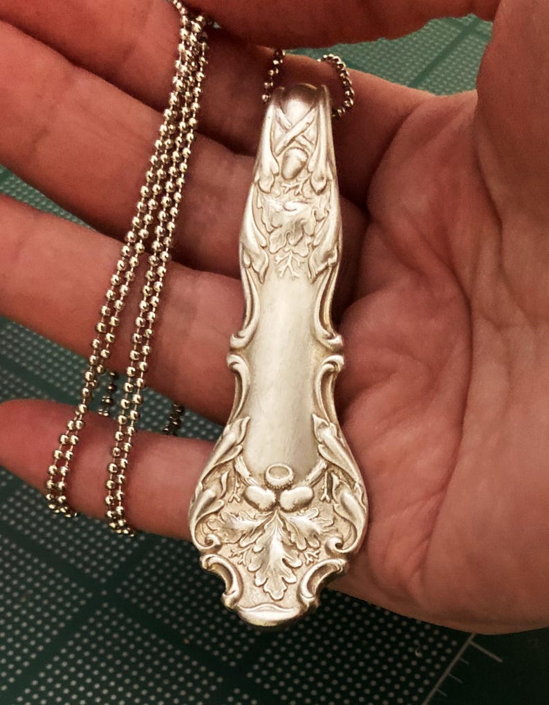 Puede incluir: Un collar de plata con un colgante hecho de una cuchara de plata vintage. La cuchara est&aacute; decorada con un dise&ntilde;o de hoja de roble y bellota.