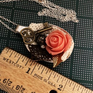 May include: A silver spoon necklace with a pink rose, a key, and lace accents. The spoon is about 2 inches long.