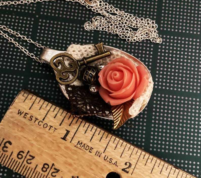 May include: A silver spoon necklace with a pink rose, a key, and lace accents. The spoon is about 2 inches long.