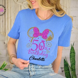 Puede incluir: Camiseta azul claro con un dise&ntilde;o brillante para un 50 cumplea&ntilde;os. El dise&ntilde;o incluye un lazo rosa, orejas de rat&oacute;n doradas, fuegos artificiales y el texto "50th Birthday Charlotte". Un regalo personalizado.