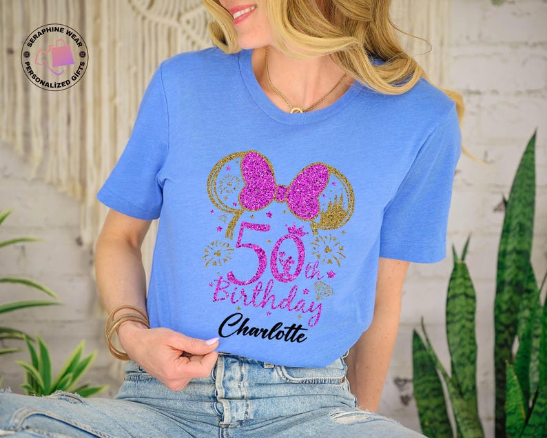 Puede incluir: Camiseta azul claro con un dise&ntilde;o brillante para un 50 cumplea&ntilde;os. El dise&ntilde;o incluye un lazo rosa, orejas de rat&oacute;n doradas, fuegos artificiales y el texto "50th Birthday Charlotte". Un regalo personalizado.
