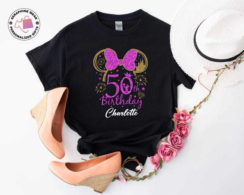 Puede incluir: Camiseta negra con un lazo morado brillante y un dise&ntilde;o de orejas doradas, celebrando un 50 cumplea&ntilde;os. La camiseta incluye el texto "50th Birthday Charlotte". Zapatos de tac&oacute;n cu&ntilde;a color melocot&oacute;n y un sombrero blanco con detalles florales.