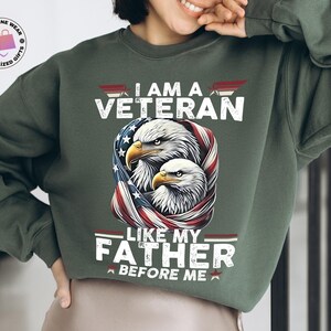 May include: Green sweatshirt featuring the text "I AM A VETERAN LIKE MY FATHER BEFORE ME" and a graphic of two eagles encircled by a US flag design. The sweatshirt is a solid green colour.