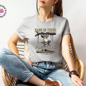 May include: A gray t-shirt with a graphic of a frog hanging on a branch with the text "Hang in there it gets worse".