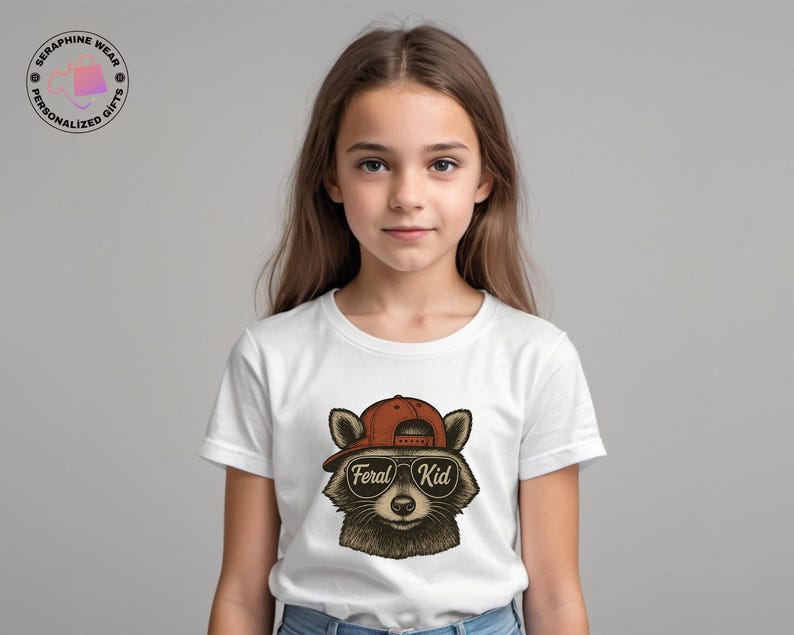 May include: A white t-shirt featuring a raccoon wearing a red cap and sunglasses. The text "Feral Kid" is printed on the sunglasses. The shirt is worn by a young person.