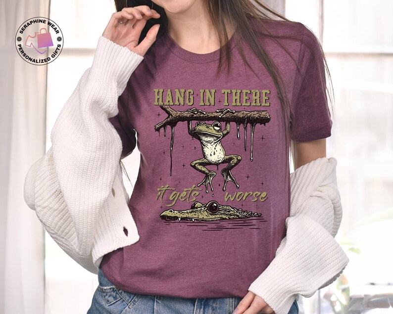 May include: A purple t-shirt with a graphic of a frog hanging from a branch with the text "Hang in there it gets worse".