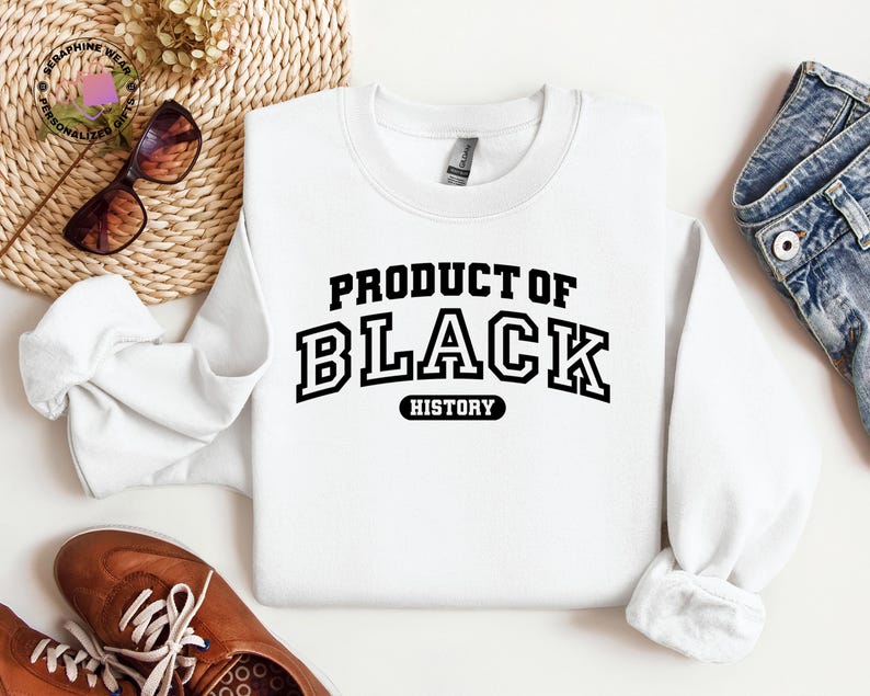 K&ouml;nnte beinhalten: Ein wei&szlig;es Sweatshirt mit dem Text "PRODUCT OF BLACK HISTORY" in fetter, schwarzer Schrift im College-Stil. Das Bild zeigt braune Schuhe, eine Sonnenbrille und Jeans.