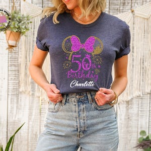 Puede incluir: Camiseta azul marino con un dise&ntilde;o brillante para un 50 cumplea&ntilde;os. El dise&ntilde;o incluye un lazo rosa, orejas de rat&oacute;n doradas, fuegos artificiales y el texto "50th Birthday Charlotte". La camiseta es de cuello redondo con mangas enrolladas.