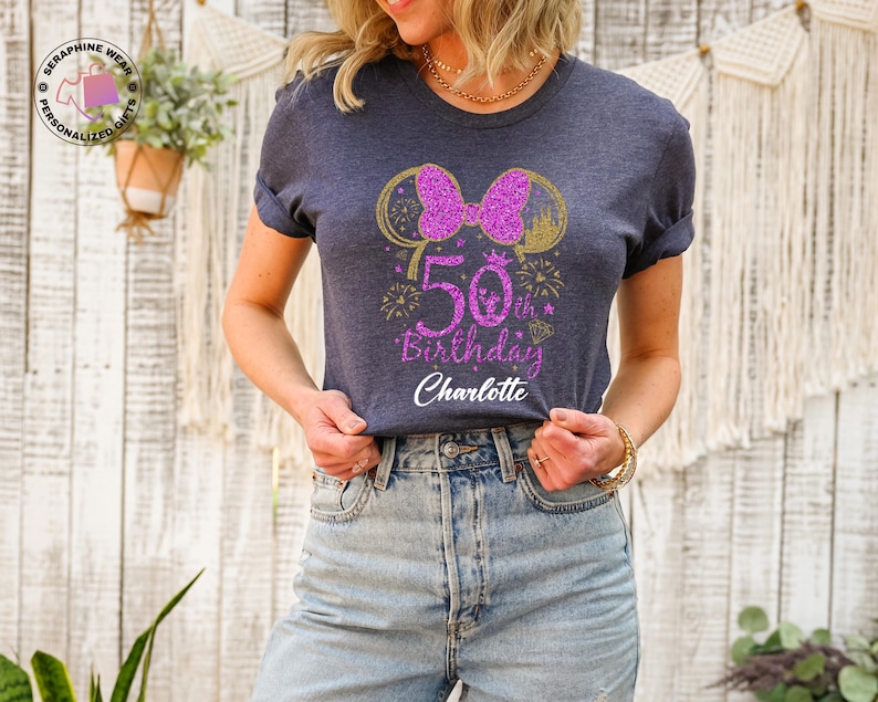 Puede incluir: Camiseta azul marino con un dise&ntilde;o brillante para un 50 cumplea&ntilde;os. El dise&ntilde;o incluye un lazo rosa, orejas de rat&oacute;n doradas, fuegos artificiales y el texto "50th Birthday Charlotte". La camiseta es de cuello redondo con mangas enrolladas.