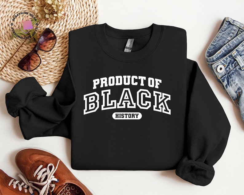 K&ouml;nnte beinhalten: Schwarzes Sweatshirt mit dem wei&szlig;en Text "PRODUCT OF BLACK HISTORY" im College-Stil. Das Bild zeigt auch braune Schuhe und blaue Jeans, was auf einen l&auml;ssigen Stil hindeutet.