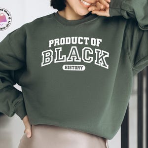 K&ouml;nnte beinhalten: Ein dunkelgr&uuml;nes Sweatshirt mit dem wei&szlig;en Text "PRODUCT OF BLACK HISTORY". Das Sweatshirt hat einen Rundhalsausschnitt und lange &Auml;rmel. Ein Logo ist in der oberen linken Ecke des Bildes zu sehen.
