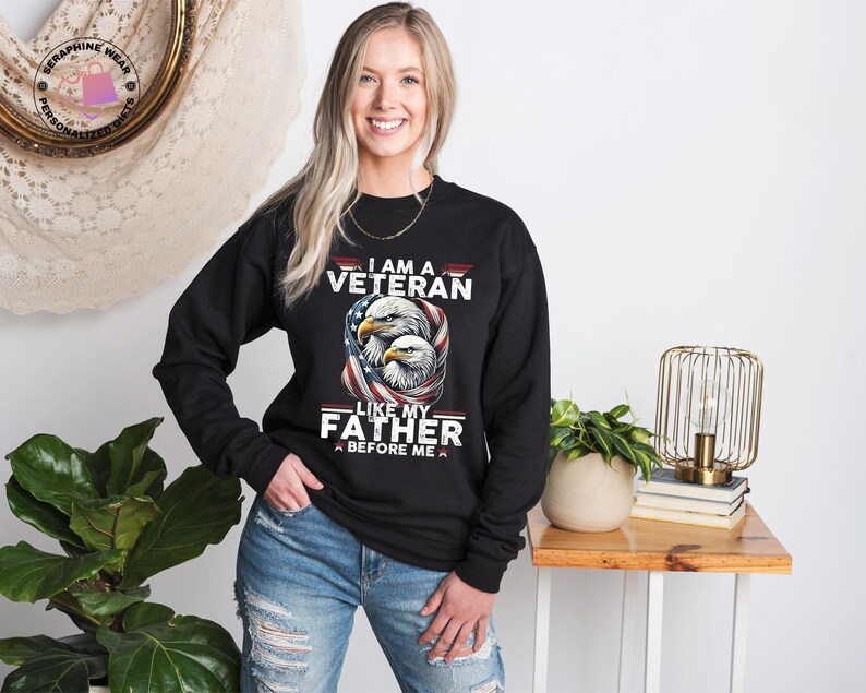 May include: Black long-sleeve sweatshirt featuring the text "I AM A VETERAN LIKE MY FATHER BEFORE ME" and an illustration of two eagles and an American flag. The sweatshirt is worn by a person.