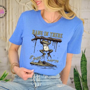 May include: A blue t-shirt with a graphic of a frog hanging on a branch with the text "Hang in there it gets worse".