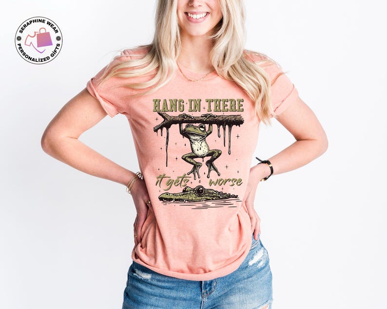 May include: A peach-colored t-shirt with a graphic of a frog hanging from a branch with the text "Hang in there it gets worse".