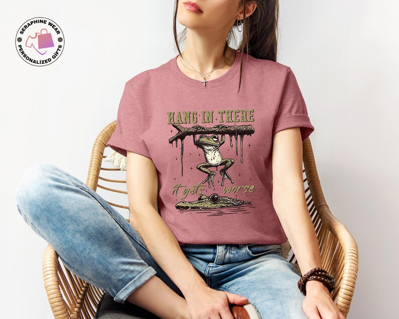 May include: A pink t-shirt with a graphic of a frog hanging on a branch with the text "Hang in there it gets worse".