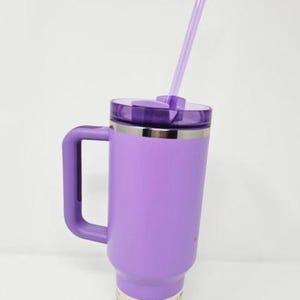 May include: A large, purple insulated tumbler with a handle and a clear straw. The tumbler has a lid and a silver band near the top. The bottom of the tumbler has a white label with icons.