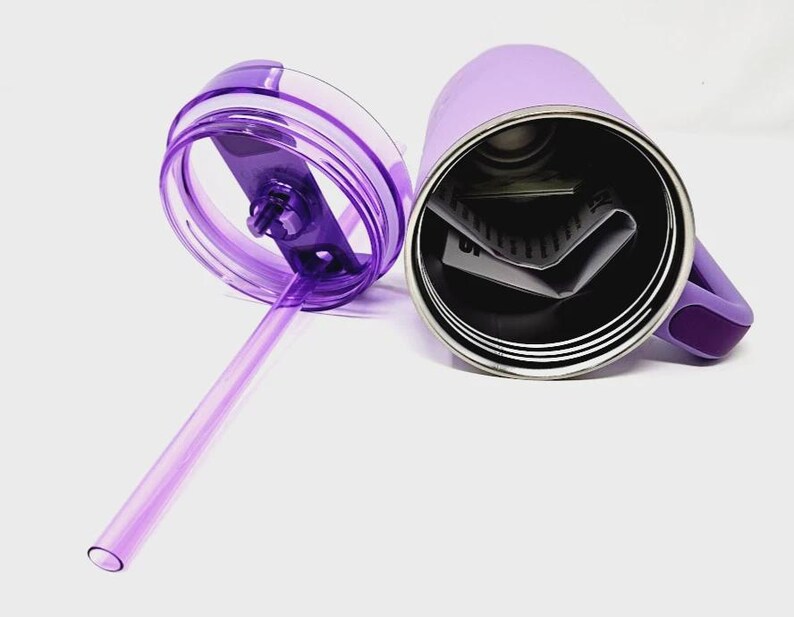 May include: A lavender-colored stainless steel tumbler with a matching handle and lid. The lid is transparent with a purple straw. The tumbler is open, revealing the interior and a few folded papers.