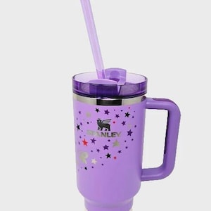 May include: A purple Stanley Quencher H2.0 tumbler with a handle and a clear straw. The tumbler features a lid, a handle, and a design of stars and the Stanley logo. The tumbler is designed for cold beverages.
