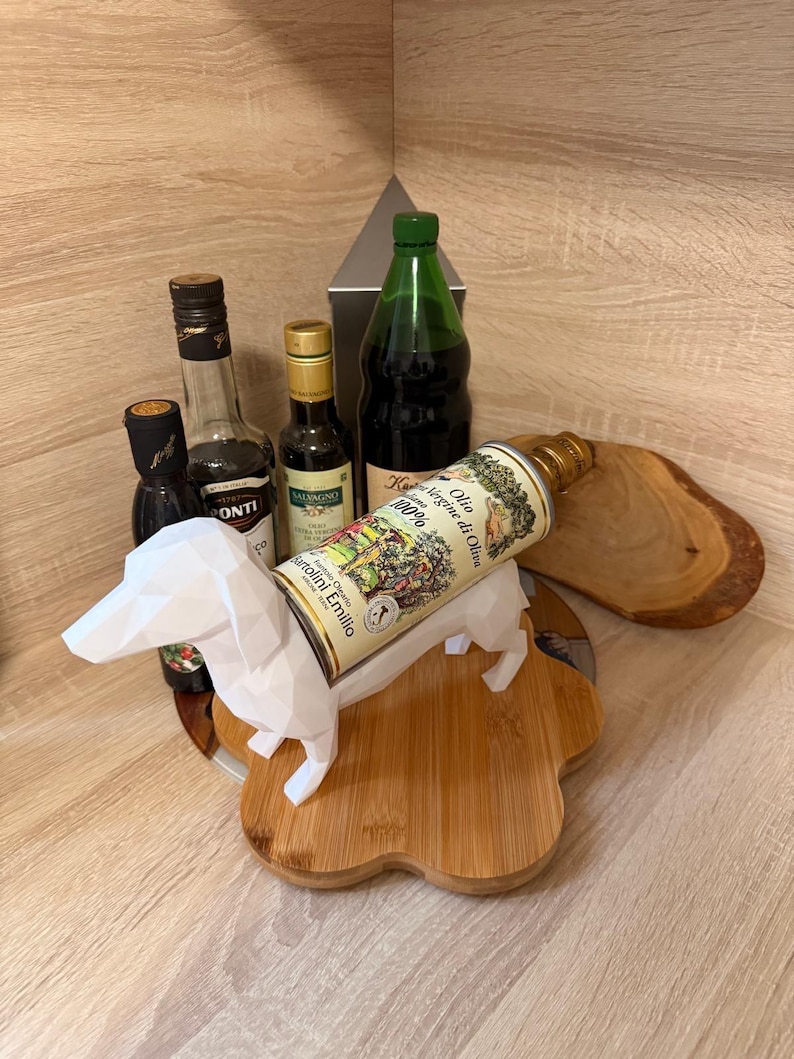 Puede incluir: Una colecci&oacute;n de botellas de aceite de oliva y vinagre, incluyendo una botella verde y una lata de aceite de oliva, exhibidas con un perro salchicha de papel blanco sobre una tabla de cortar de madera. La lata de aceite de oliva dice "Olio Extra Vergine di Oliva".