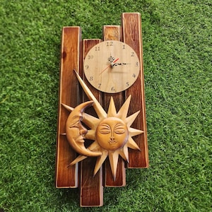 Puede incluir: Un reloj de pared de madera con un diseño de sol y luna. La esfera del reloj es redonda y tiene números romanos. Las manecillas del reloj son negras y rojas.