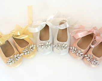 May include: Four pairs of sparkly baby shoes with satin ribbon ties. The shoes are in gold, silver, and pink.