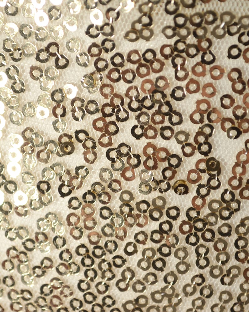Op de afbeelding: Close-up van een stof bedekt met gouden pailletten. De pailletten zijn gerangschikt in een herhalend patroon.
