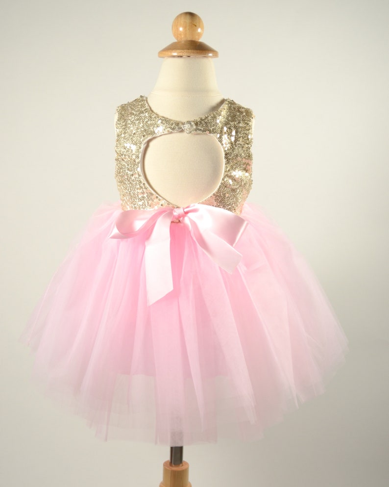 Op de afbeelding: Een roze tule tutu-jurk met een gouden pailletten-lijfje en een hartvormige uitsnijding in de rug. De jurk heeft een roze satijnen strik in de taille.