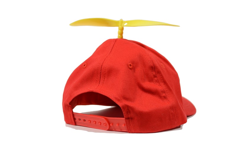 May include: A red baseball cap with a yellow propeller on top. The cap has a velcro strap on the back.