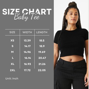 Puede incluir: Una camiseta negra con una tabla de tallas en pulgadas. La tabla enumera las tallas XS a 2XL, con las medidas correspondientes de ancho y largo. La modelo lleva la camiseta negra y un pantal&oacute;n a rayas negras.