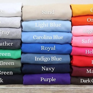 K&ouml;nnte beinhalten: Ein Stapel gefalteter Stoffe in verschiedenen Farben, darunter Wei&szlig;, Aschgrau, Sportgrau, Dunkelgrau und Schwarz. Weitere Farben sind Sand, Hellblau, Royalblau, Marineblau und Lila. Das Bild zeigt auch Gold, Orange, Hellrosa, Rot und Kastanienbraun.
