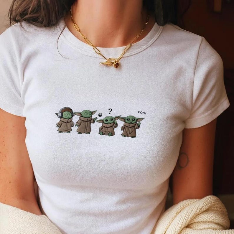 May include: White t-shirt featuring a cartoon design of four Grogu characters in different poses. The first Grogu wears headphones, the second holds a ball, the third has a question mark, and the last says "cool!"