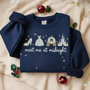 Puede incluir: Sudadera azul marino con un dise&ntilde;o tem&aacute;tico de Cenicienta. El dise&ntilde;o incluye un tac&oacute;n alto, un vestido de baile, un carruaje y un castillo, con el texto "meet me at midnight". La sudadera est&aacute; decorada con detalles dorados y cruces.
