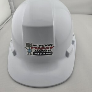 May include: A white hard hat with a sticker that reads "IF YOUR PUSSY HURTS JUST STAY HOME". The sticker features a cartoon cat character. The hard hat is a standard safety helmet.