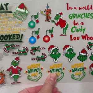 May include: A clear sheet with various Grinch-themed stickers. The stickers include the Grinch, Cindy Lou Who, candy canes, and ornaments. Text includes "My Day", "I'm Booked!", and "In a world full of GRINCHES, be a Cindy Lou Who."