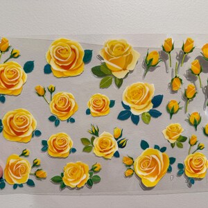 Puede incluir: Una hoja de pegatinas de rosas amarillas con hojas verdes y capullos amarillos. Las pegatinas presentan rosas de varios tamaños, desde completamente florecidas hasta capullos apretados. Las rosas tienen un degradado de amarillo y naranja.