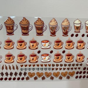 May include: A sheet of stickers featuring various coffee and latte designs. The stickers are in shades of brown, beige, and white. There are also small heart, leaf, and coffee bean stickers.