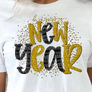 Może przedstawiać: Biała koszulka z grafiką "Happy New Year". Tekst zawiera połączenie złota i czerni, a słowo "New" ma czarny wzór w kratę. Złote konfetti otacza tekst, tworząc świąteczny design.